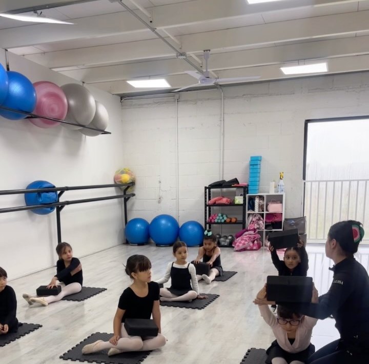 Niñas en tapetes durante una clase de pre-ballet con su maestra.